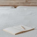 Open blank notepad with pen on creased bed sheet with ornament in light bedroom